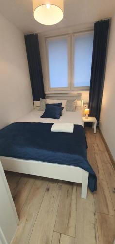 a bedroom with a bed with blue sheets and two windows at Apartament Roanta in Polanica-Zdrój