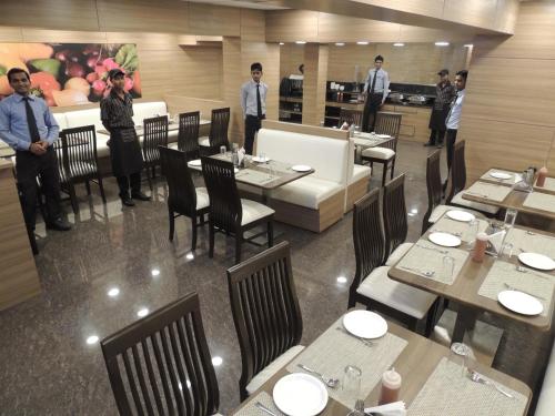 a restaurant with tables and chairs and people standing around at Central Beacon Hotel in Surat