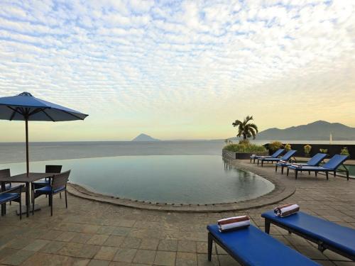 a resort with a pool and chairs and an umbrella at Aryaduta Manado in Manado