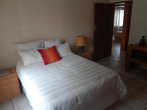 a bedroom with a white bed with a red pillow at VILLA LA CORRIE Guest Lodge in Steelpoort