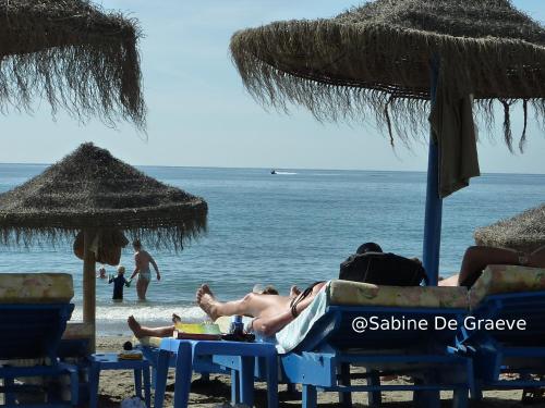 Ein Mann, der unter Sonnenschirmen am Strand liegt. in der Unterkunft Primera línea de playa, deditos de los pies en la arena !! Carabela-C704 Piscina Torrox-Costa in Torrox Costa