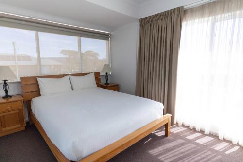 a bedroom with a white bed and a large window at Amooran Oceanside Apartments and Motel in Narooma