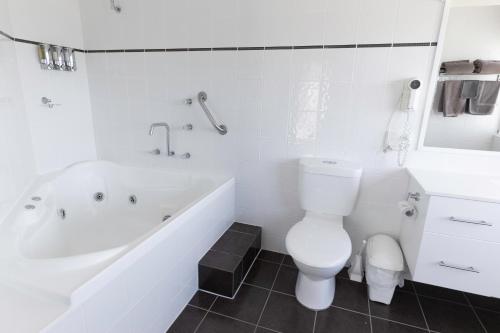 a white bathroom with a toilet and a bath tub at Amooran Oceanside Apartments and Motel in Narooma