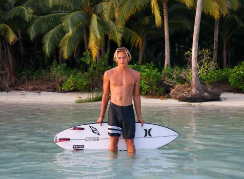 a man standing in the water with a surfboard at Diamond Island Eco Resort in Pulau Palambakbesar
