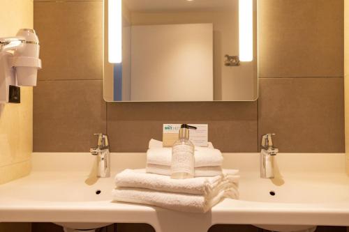 a bathroom with a sink with towels and a mirror at Brit Hotel Ploermel - Hotel de l'Hippodrome in Ploërmel