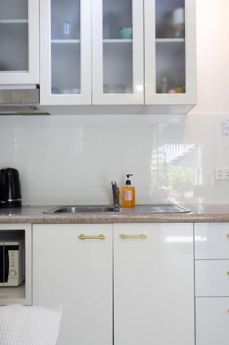 a white kitchen with white cabinets and a sink at Zen Escape Guest House " Location 2" - Zen Garden Tiny Home, Nooky Studio, Chillax Rest in Brisbane