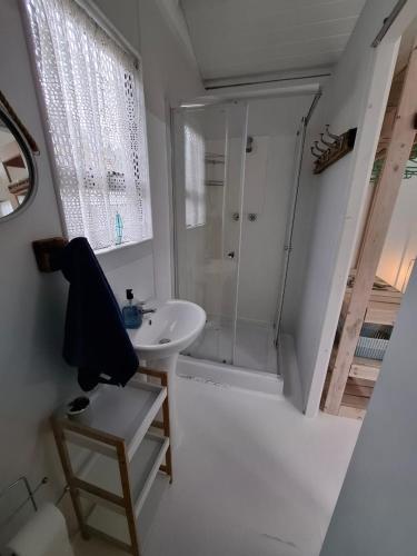 a white bathroom with a shower and a sink at Petite Cottage Plett in Plettenberg Bay
