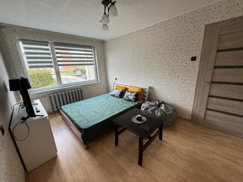a bedroom with a bed with a table and a window at Vieno kambario apartamentai Telšiuose in Telšiai