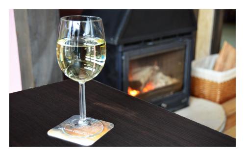 a glass of wine sitting on a table with a fireplace at Pensiunea Bia Papadia in Bicaz