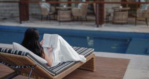 a woman sitting in a chair reading a book by a pool at Aahana Resort - Jim Corbett in Rāmnagar
