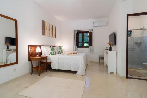 a white bedroom with a bed and a bathroom at Pousada Samambaia in Trancoso