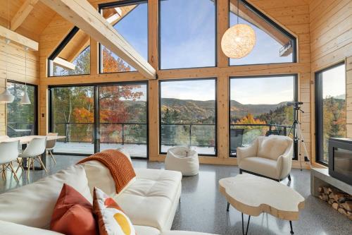 a living room with white furniture and large windows at Le Harfång - Vue imprenable - Sauna - 3min du Mont in LʼAnse-Saint-Jean