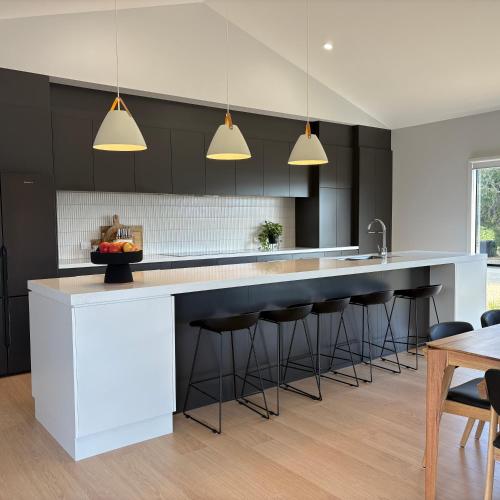 a kitchen with black cabinets and a white island with bar stools at Goolwa Beach Pavilion in Goolwa South