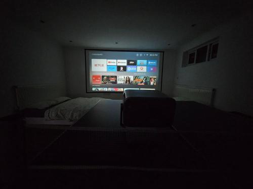 a dark room with a bed and a large screen television at Large Annexe with games room pool table ping pong air hockey movie projector in Windsor