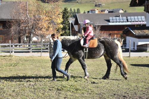 a woman walking a horse with a little girl on it at Obenfigerhof in Kals am Großglockner