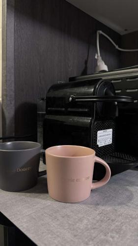 two coffee cups sitting on a counter next to a toaster at Appartement cosy et chaleureux avec vue sur nature in Liancourt