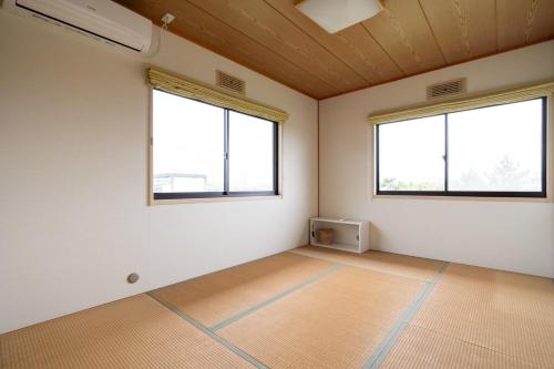 an empty room with two windows and a wooden ceiling at Hamanoakariya Kujukuri in Katakai