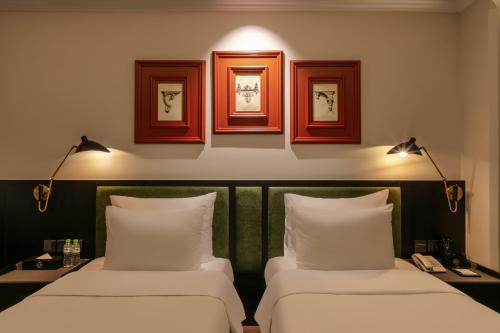 two beds in a room with three pictures on the wall at Champton Hanoi Hotel in Hanoi