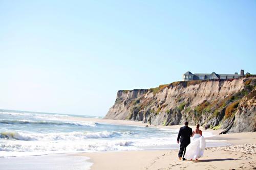a bride and groom walking on the beach at The Ritz-Carlton, Half Moon Bay in Half Moon Bay