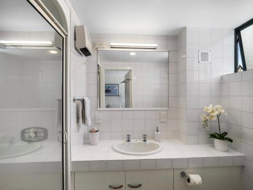 a white bathroom with a sink and a mirror at Poolside Waterfront - Orewa Oceanside Villa in Orewa