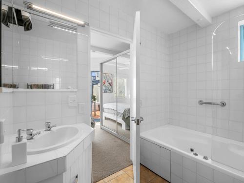 a white bathroom with a tub and a sink at Poolside Waterfront - Orewa Oceanside Villa in Orewa