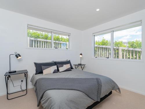a white bedroom with a bed and two windows at Greenhills Charmer - Coromandel Town Holiday Home in Coromandel Town