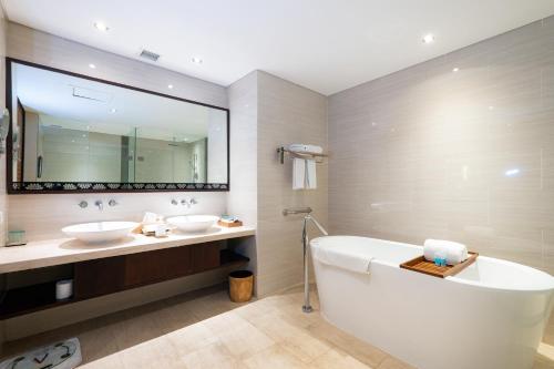 a bathroom with two sinks and a tub and a large mirror at VOUK Hotel and Suites Nusa Dua Bali in Nusa Dua