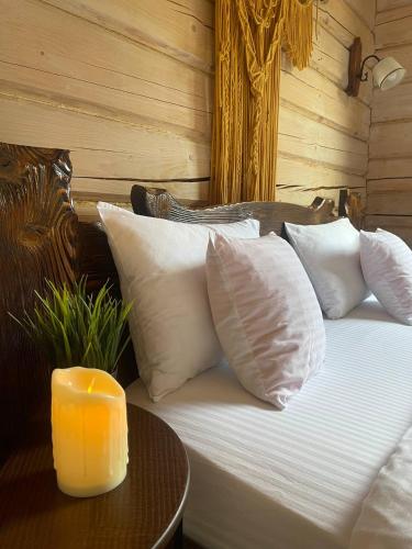 a bed with white pillows and a candle on a table at Над фермою in Nizhne-Studënyy