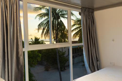 1 dormitorio con ventana y vistas a una palmera en Mathiveri Cool Breeze, en Mathiveri
