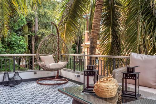 a balcony with a swing and a chair and palm trees at Villa Stairway to Heaven by tisyastays in Candolim