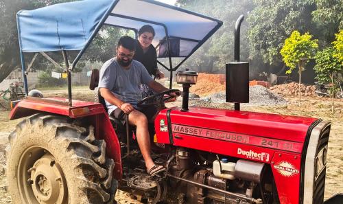 two men are sitting on a red tractor at Shobhayan inn, airport railway station pickup free in Ayodhya