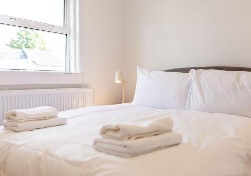 a white bed with towels on it with a window at Bright & Airy 2BD - 10 mins walk to Chelt Centre! in Cheltenham