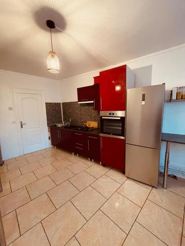 La cuisine est équipée de placards rouges et d'un réfrigérateur en acier inoxydable. dans l'établissement Jolie-maison-en-centre-ville, à Brébières