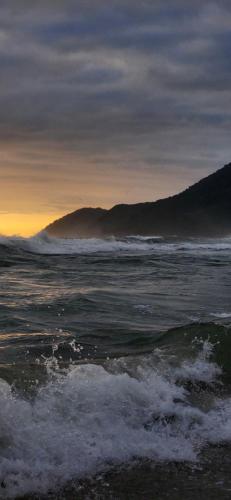 a beach with waves in the ocean at sunset at Pousada Pitaya Maresias in Maresias