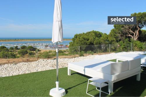 a white bed and an umbrella on the grass at Garden Playanatural - Adults Only in El Rompido