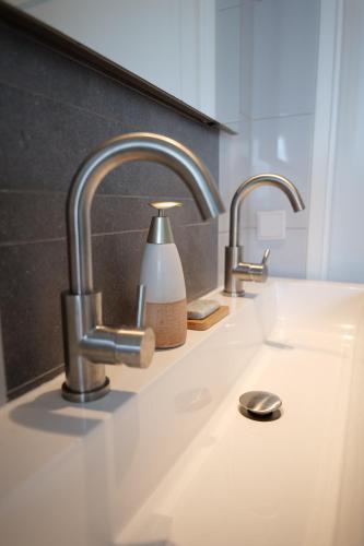 a bathroom sink with two faucets and a bottle of soap at Bed & breakfast by Patty in Nieuw-Amsterdam