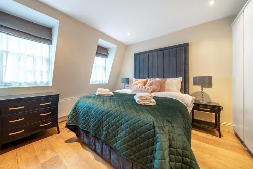 a bedroom with a bed with a green comforter and two windows at The Mayfair Residence in London