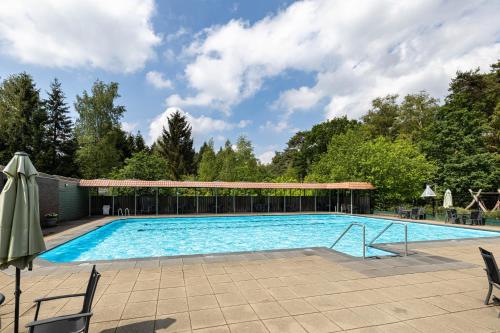 a large swimming pool with chairs and a building at Luxe familiehuis in parkbos in Giethmen