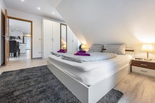 a white bedroom with a large white bed with purple pillows at To Huus am Steinhuder Meer in Steinhude