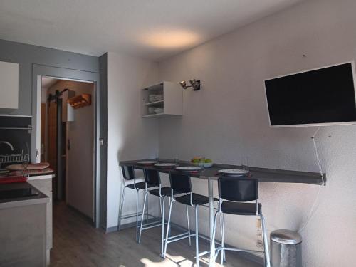 a kitchen with a bar with stools and a television on the wall at Location semaine 7 nuits du samedi au samedi Studio 20m2 cozy 4pers au pied d une piste bleu accès remontés in Valfréjus