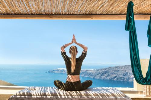 a woman doing yoga on a bed in front of a window at Andronis Concept Wellness Resort in Imerovigli