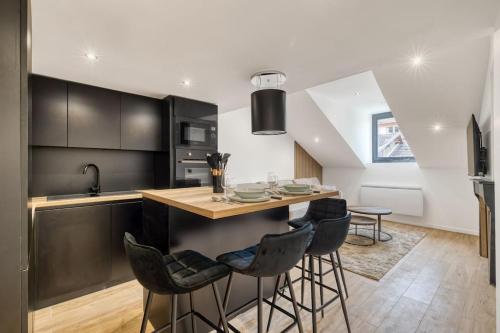 une cuisine avec des placards noirs et un îlot avec des tabourets de bar dans l'établissement Le Duplex, à Évian-les-Bains