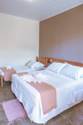 two beds in a bedroom with white sheets and flowers on them at Pousada Porto Da Barra in Porto Seguro