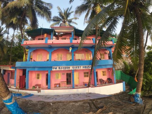 a pink and blue building with palm trees at Om Ganesh Guest House Cliffside in Arambol