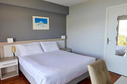 a bedroom with a white bed with a desk and a chair at Hôtel Alexandra in Roquebrune-Cap-Martin