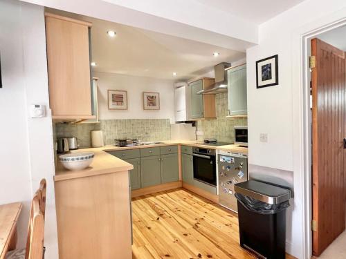 a kitchen with green cabinets and a wooden floor at 3 bedroom barn conversion with swimming pool, tennis court and more! in Kingsbridge