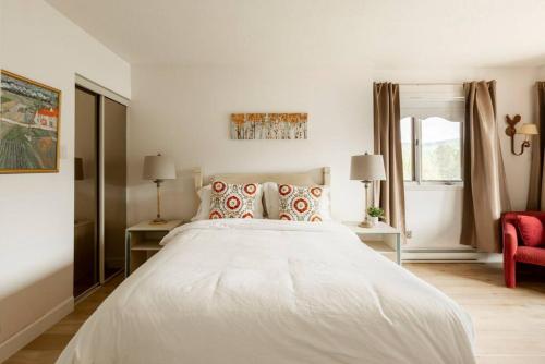 a white bedroom with a large bed and a red chair at InstantSuites- The Mountain Lake house in Mont-Tremblant