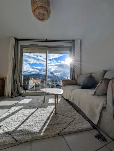 - un salon avec un canapé et une table en face d'une fenêtre dans l'établissement Studio Confortable & Lumineux - Vue Montagne & Lac - Plan d'Eau, à Embrun