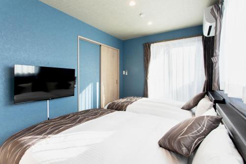 a bedroom with two beds and a tv on the wall at 貸し切り宿 世紡 YOTSUMUGI sakazuki and iyasaka in Yufuin