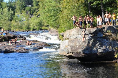 a group of people jumping off a rock into a river at Au Chic Chalet des Chutes Chic Rustique in Sainte-Melanie